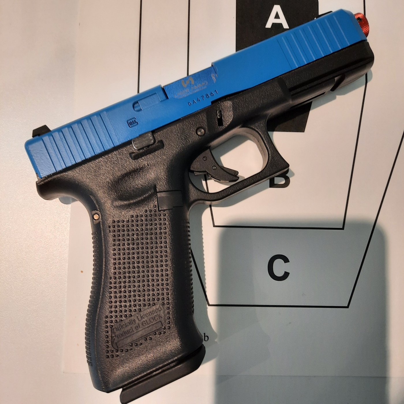 A blue-slide, officially licensed Glock 17 laser training pistol resting on a scoring target.